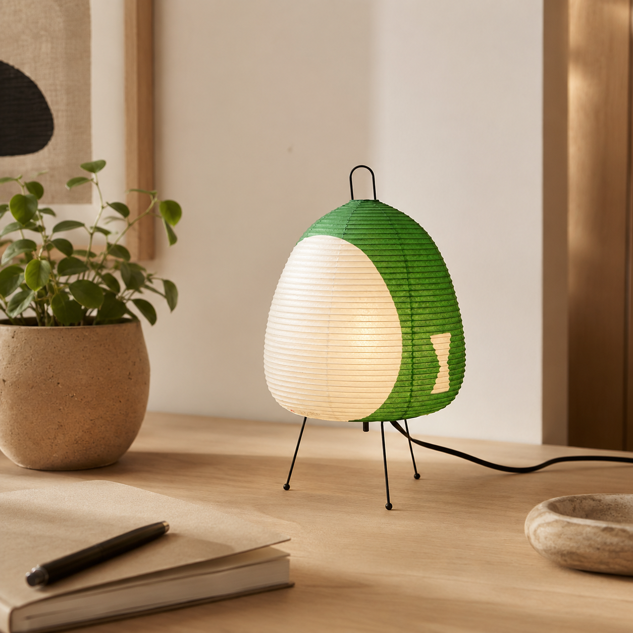 Green and white lamp on a wooden surface with a plant and notebook in the background